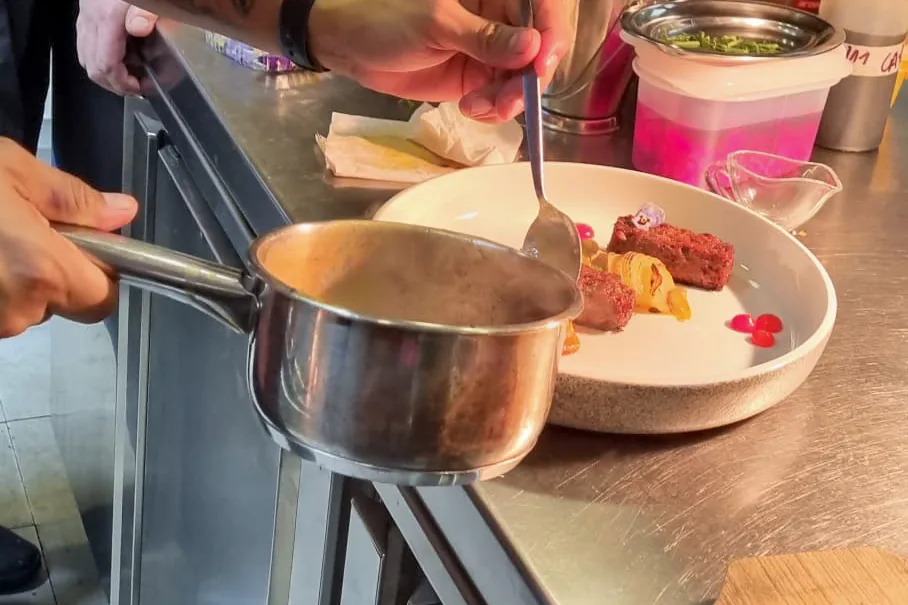 Júnior Machado termina un plato con una salsa, en el pase de una cocina en servicio