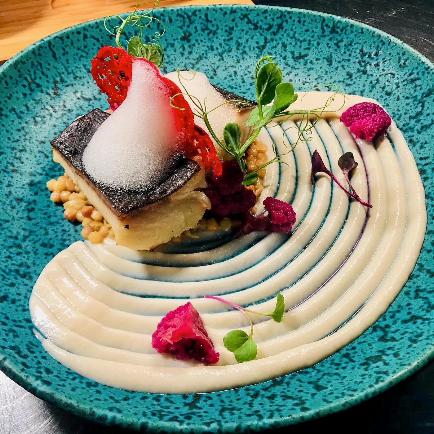 Pescado con espuma y crema sobre un plato turquesa